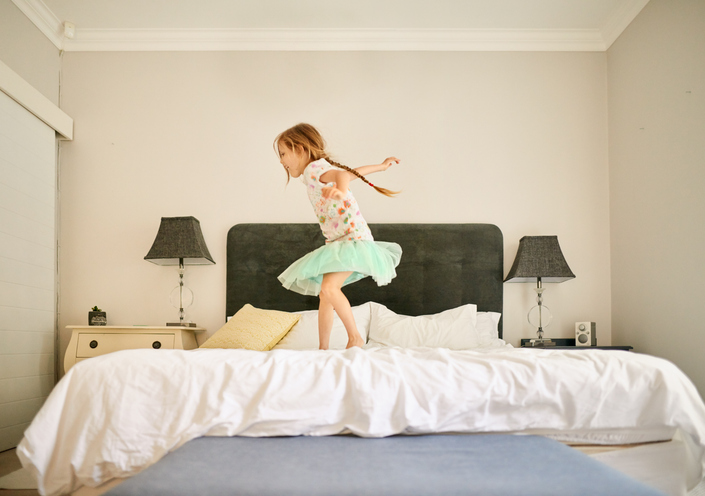 Laughing little girl jumping on her parent's bed